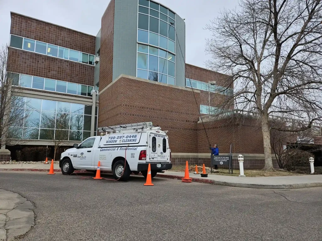 Metropolis service truck parked with safety cones setup outside a multi-story brick commercial facility during an exterior window cleaning project